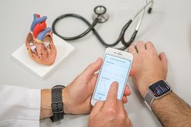 Smartphone des Arztes und Smartwatch eines Patienten mit Daten zur Herzfunktion