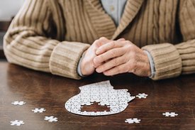 Hände eines alten Menschen über einem unfertigen Puzzle