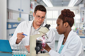 Ein älterer hellhäutiger Forscher und eine junge afrikanische Forscherin arbeiten mit einem mikroskop in einem Labor.