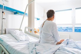 Patient in OP-Kleidung sitzt auf Klinikbett