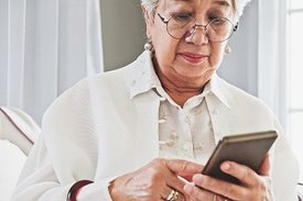 Eine Seniorin schaut auf ihr Mobiltelefon.