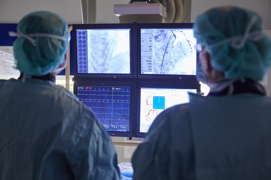 Zwei Ärzte in OP-Kleidung betrachten Bildschirm-Aufnahmen einer Herzkatheter-Untersuchung.