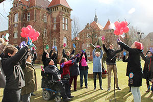Fröhliche Menschen mit roten Luftballons und bunten Handschuhen winken.