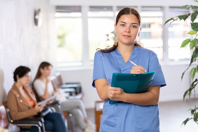 Eine Ärztin macht sich Notizen in einem Warteraum, im Hintergrund sitzen zwei Patientinnen