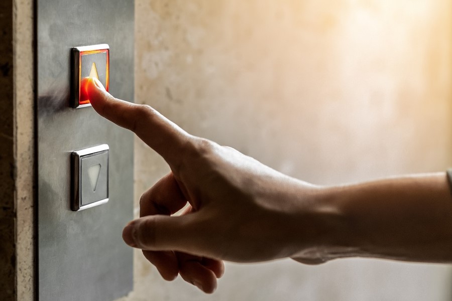 Eine Person drückt mit dem Zeigefinger auf einen Aufzugknopf